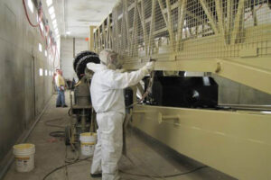 Employee applying ZERUST Axxanol Spray-G rust preventative grease on large equipment for corrosion protection.