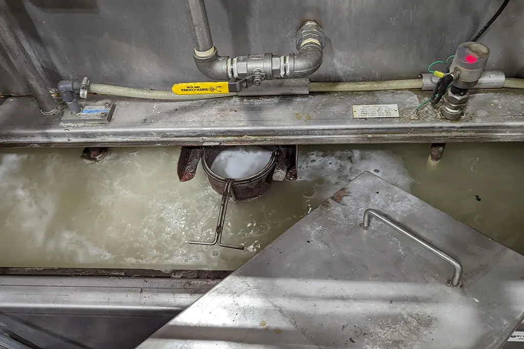Low foam metal cleaner in industrial holding tank with minimal foam buildup during operation
