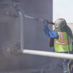 Worker performing wet blasting on a tank wall before painting
